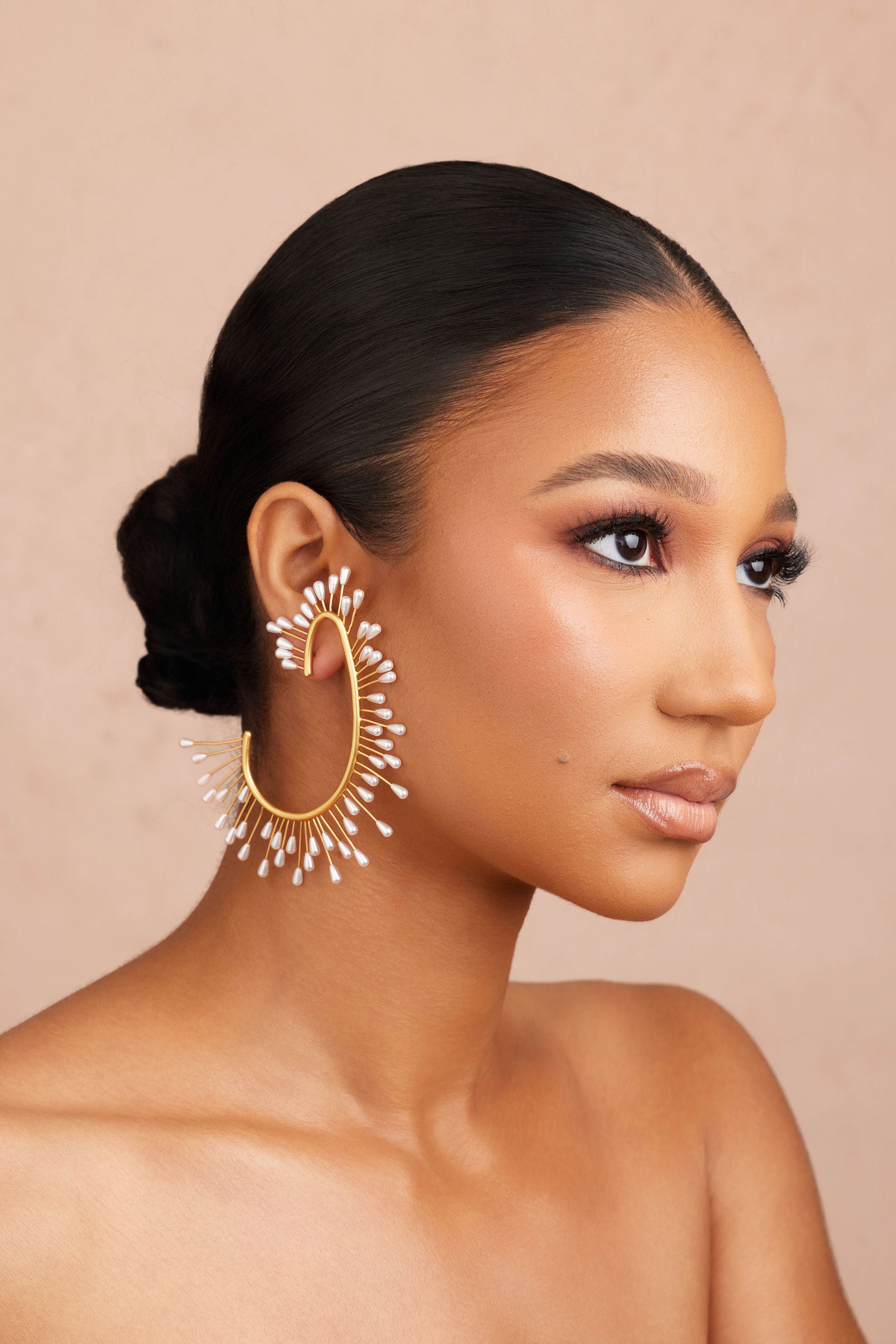 Woman wearing large gold hoop earrings with a beige background