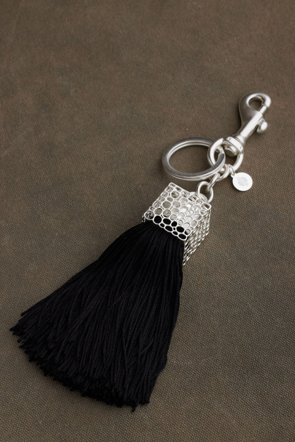 Black tassel keychain with silver clasp on a brown background