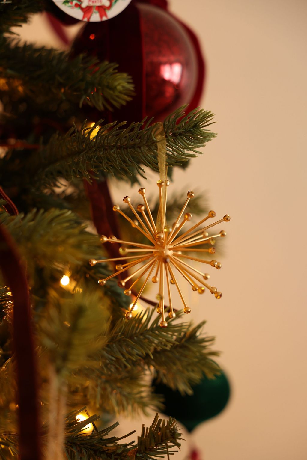 Gold star-shaped ornament on a Christmas tree with a red ornament in the background.