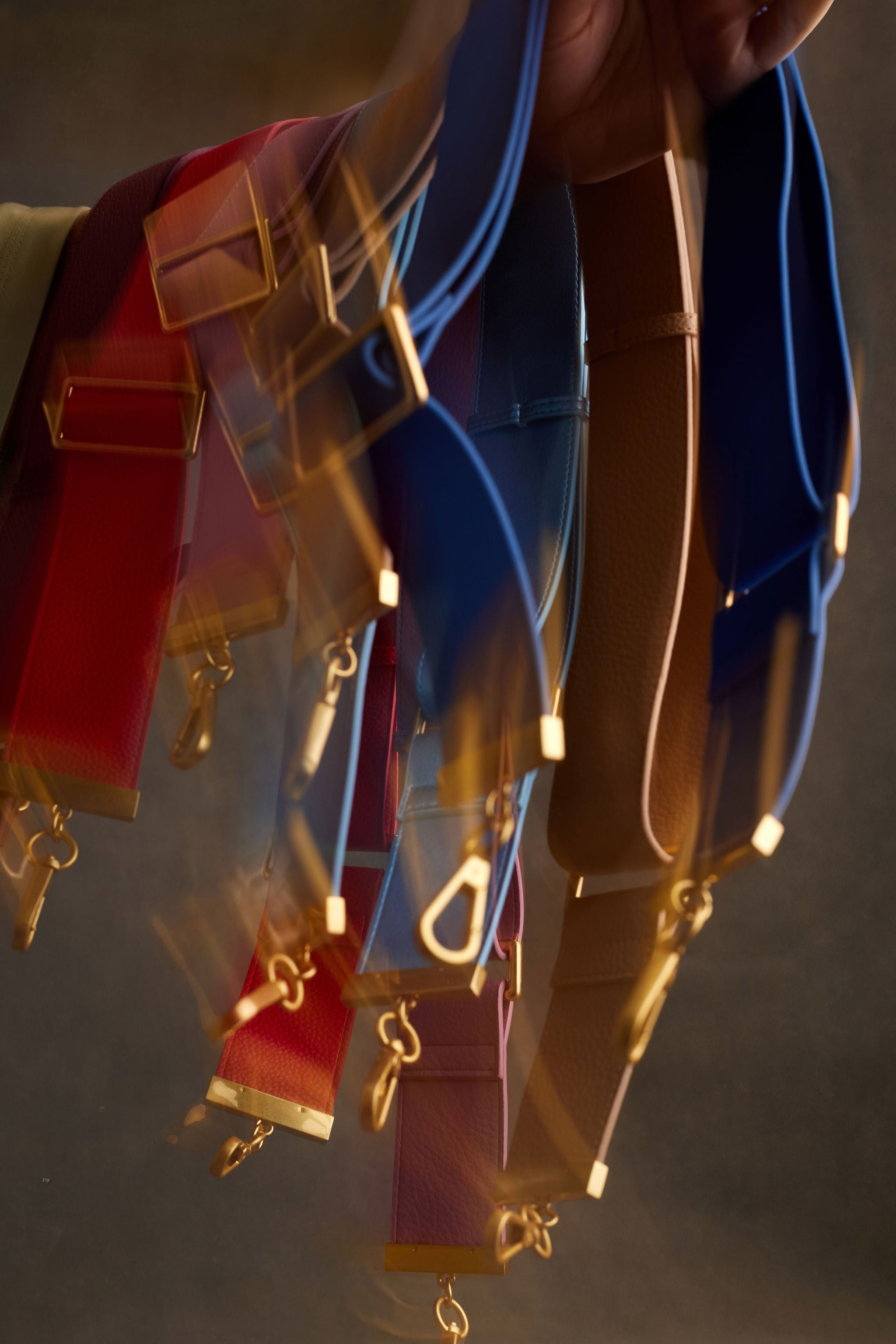 Close-up of colorful leather belts with gold buckles on a neutral background