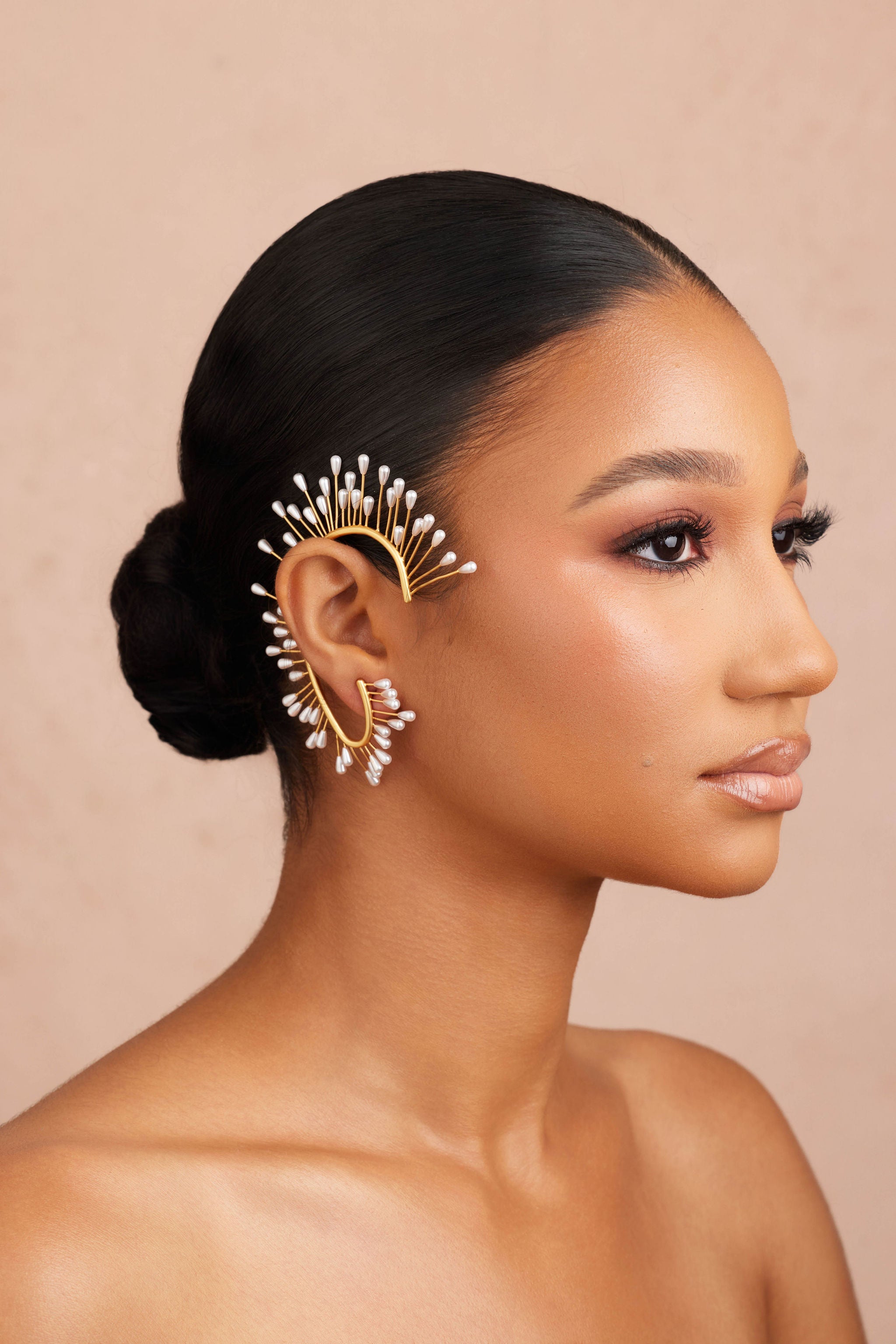 Woman wearing a gold earring with a beige background