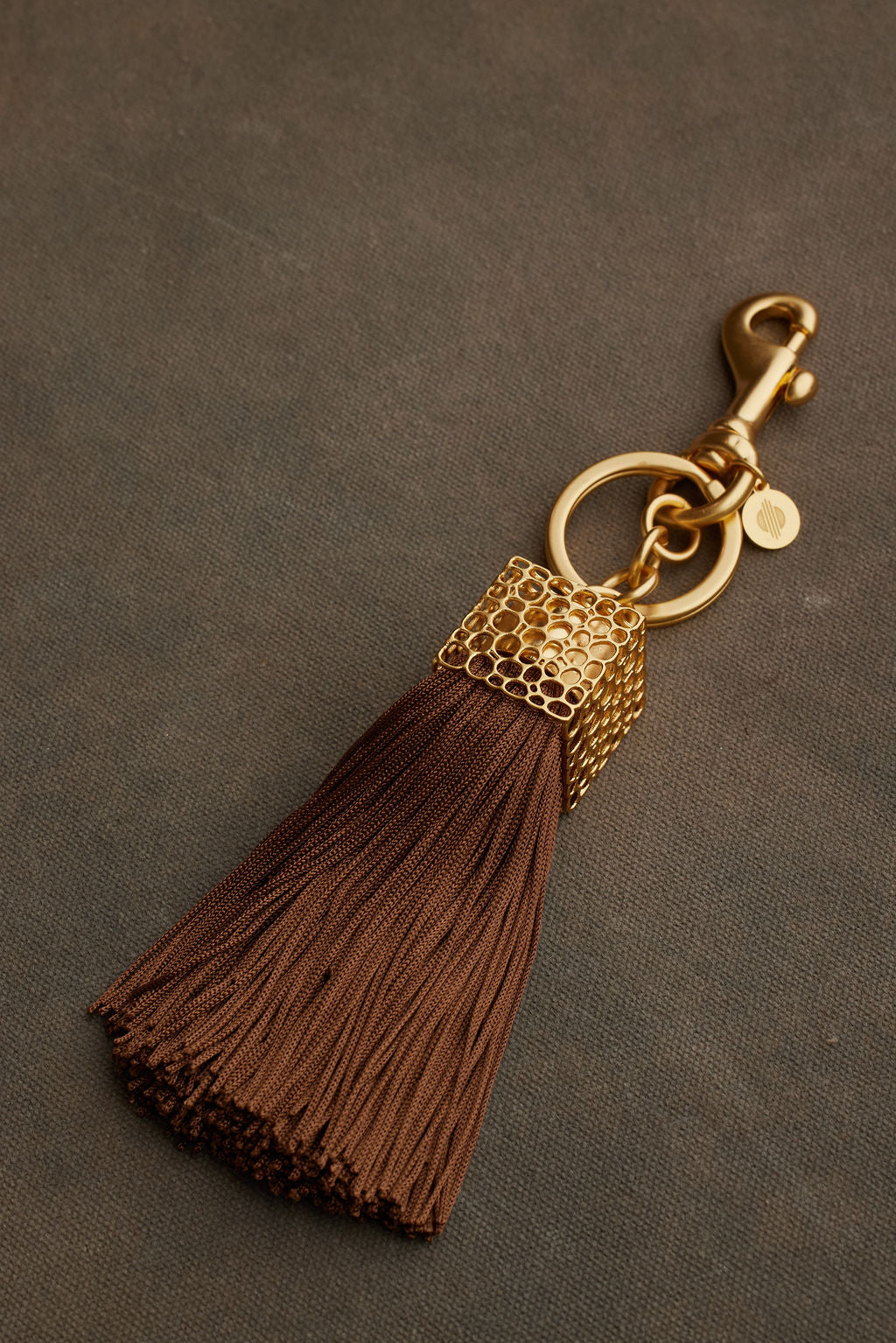 Brown tassel keychain with gold metal accent on a dark background
