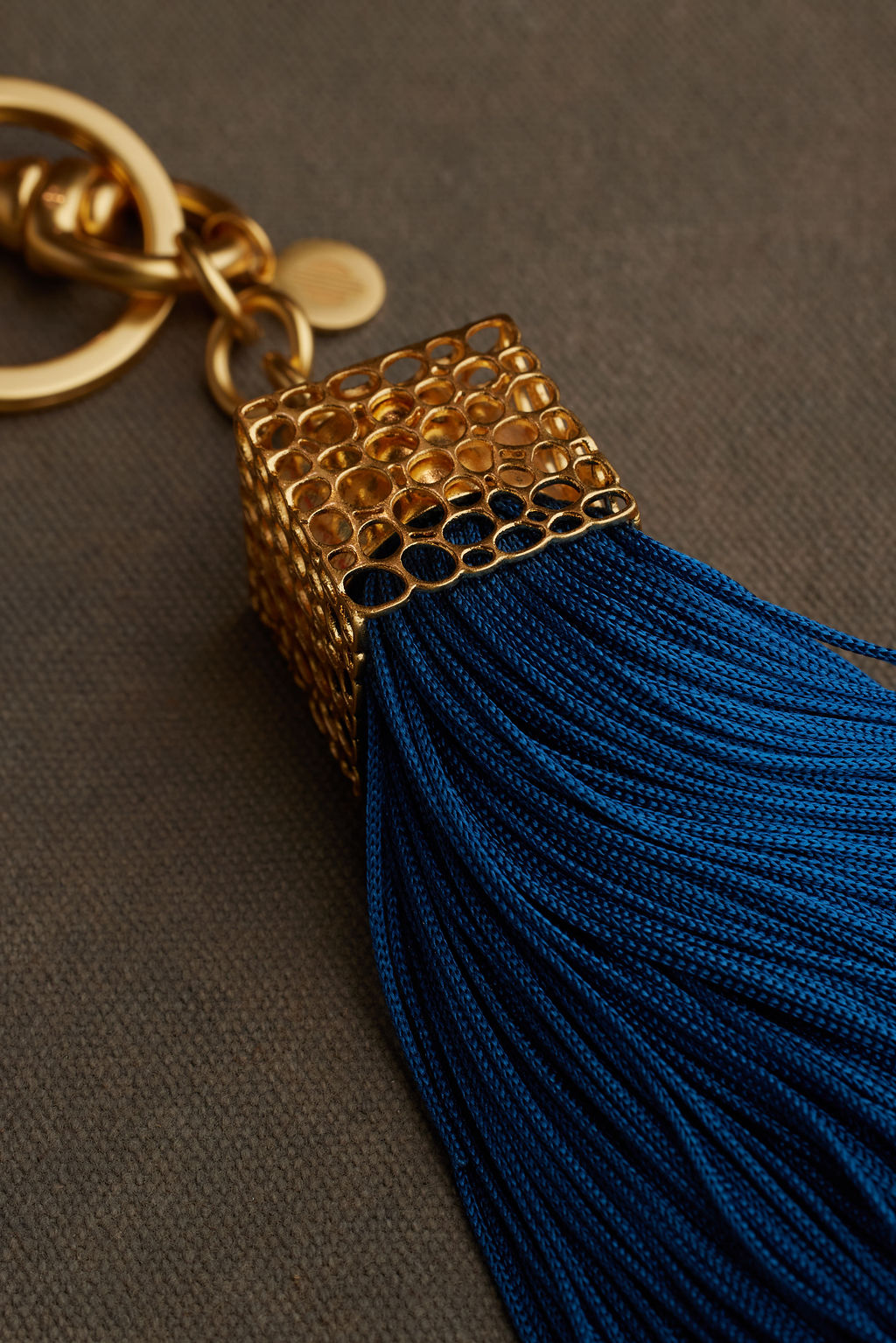 Gold keychain with a blue tassel on a gray background