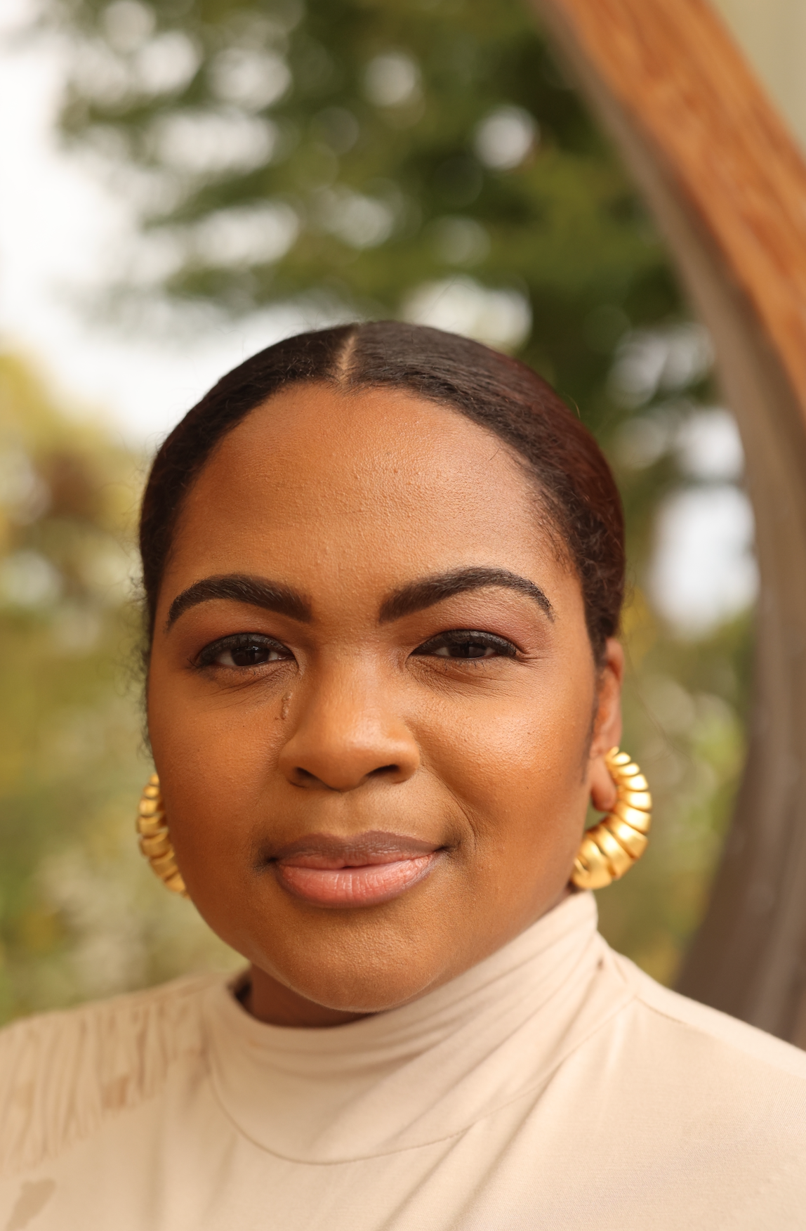 A close-up image of a person wearing a beige sweater and gold-colored earrings.