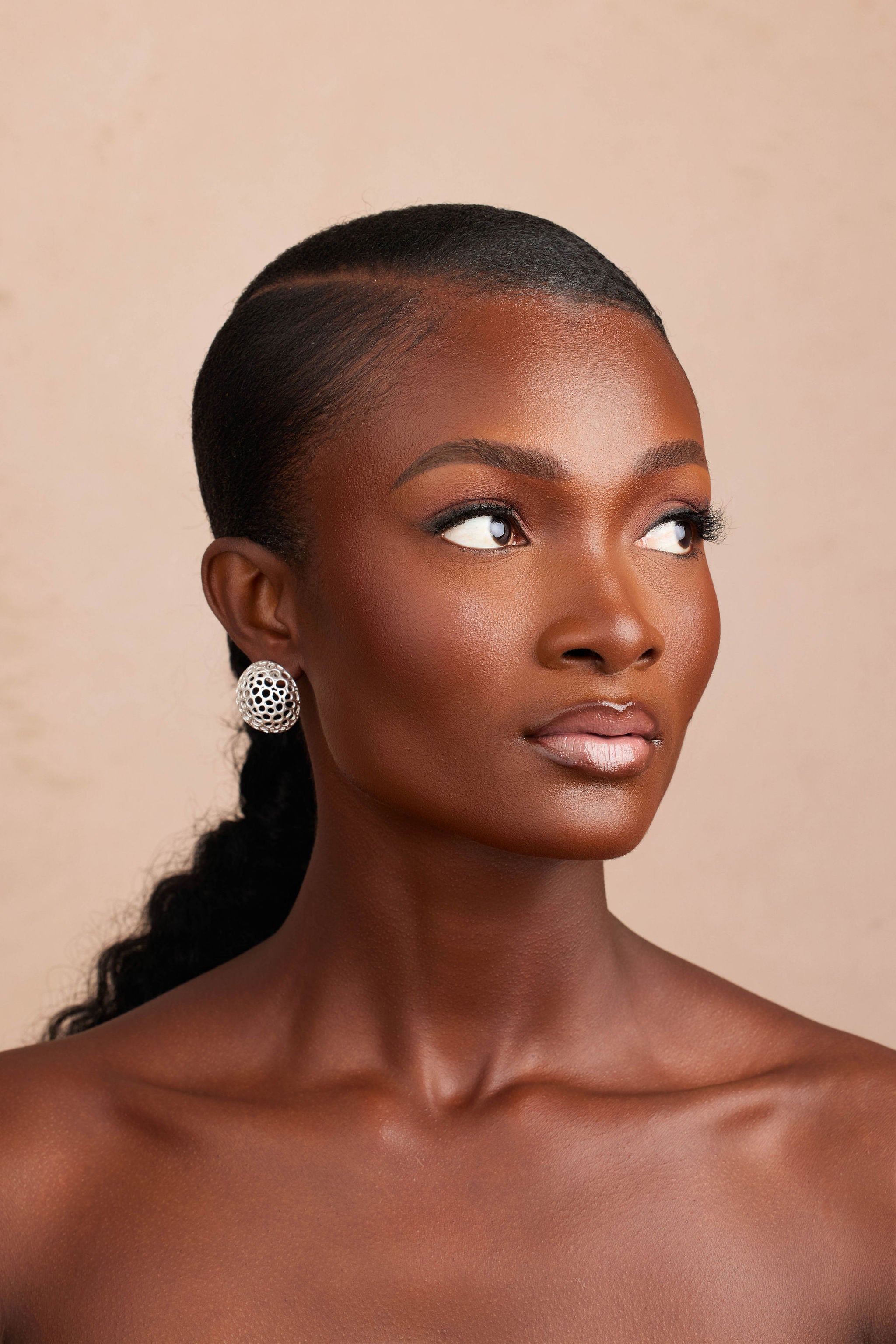 Woman with styled hair and earrings against a beige background