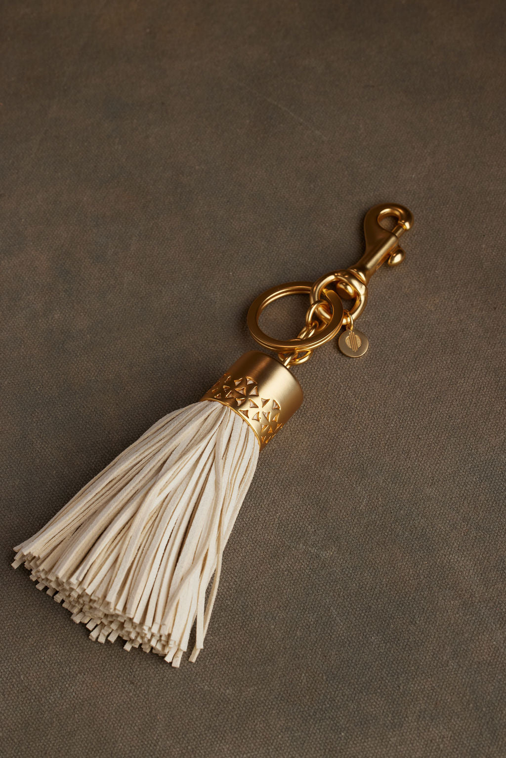White tassel keychain with gold accent on a brown background